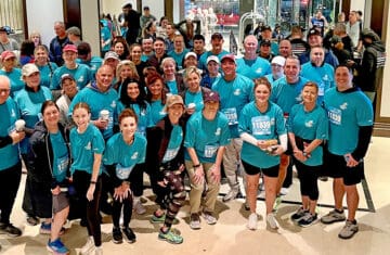 A large group of volunteers wearing matching teal shirts poses together indoors after participating in the Tunnel to Towers 5K in New York City.