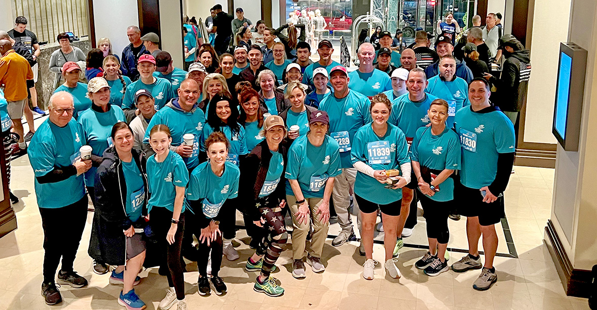 A large group of volunteers wearing matching teal shirts poses together indoors after participating in the Tunnel to Towers 5K in New York City.